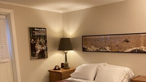 Et soveværelse med en stor seng, et natbord, en lampe, et plakat og et billede på væggen.