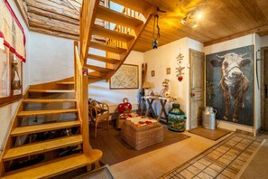 Una escalera de madera conduce a un dormitorio tipo loft con una decoración rústica, que incluye un cuadro de vaca y un techo de madera.