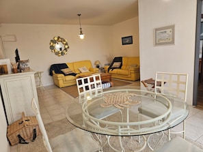 A living room with a yellow sofa, a glass table, and a white chair.
