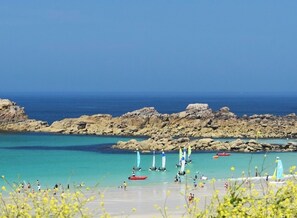 A beach with clear turquoise water, rocky formations, and sailboats.