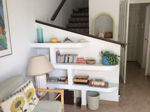 Cozy living space with a staircase leading to an upper level featuring a comfortable chair and a small table with a basket and books.