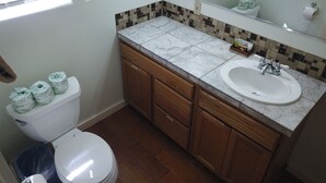Baño con inodoro, lavabo, armarios de madera y salpicadero de azulejos.