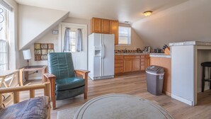 Una cocina acogedora con armarios de madera, un refrigerador y un comedor con una silla y una mesa.