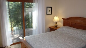 Ein Schlafzimmer mit einem Bett, einem Nachttisch mit Lampe, einem Fenster mit Vorhängen und einem gerahmten Bild an der Wand.
