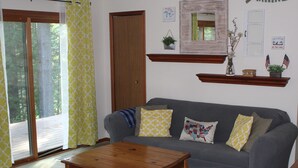 Ein Wohnzimmer mit grauem Sofa, Couchtisch aus Holz und einem Fenster mit gelb gemusterten Vorhängen.