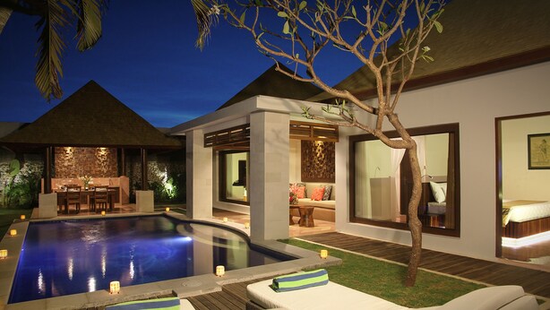 Un área de piscina moderna al aire libre con sillones de descanso, un conjunto de comedor y un espacio interior bien iluminado.