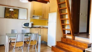 A compact kitchen with a dining table and chairs, a microwave, and a refrigerator. There is a wooden staircase leading to another level. - Bellevue by Interhome (Sierra Nevada)