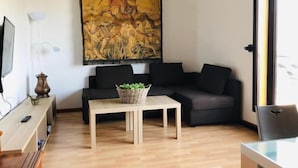 A modern living room with a sofa, a small table with a basket, a TV, and a painting on the wall. - Bellevue by Interhome (Sierra Nevada)