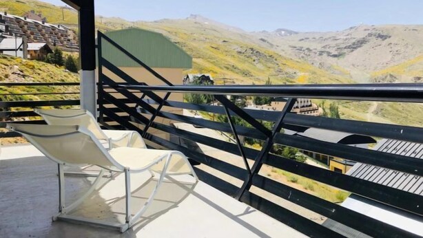 A balcony with a white chair, a metal railing, and a view of a mountainous landscape. - Bellevue by Interhome (Sierra Nevada)