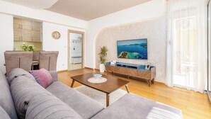 Een moderne woonkamer met een grijze bank, een houten salontafel, een aan de muur bevestigde televisie en een houten kast.