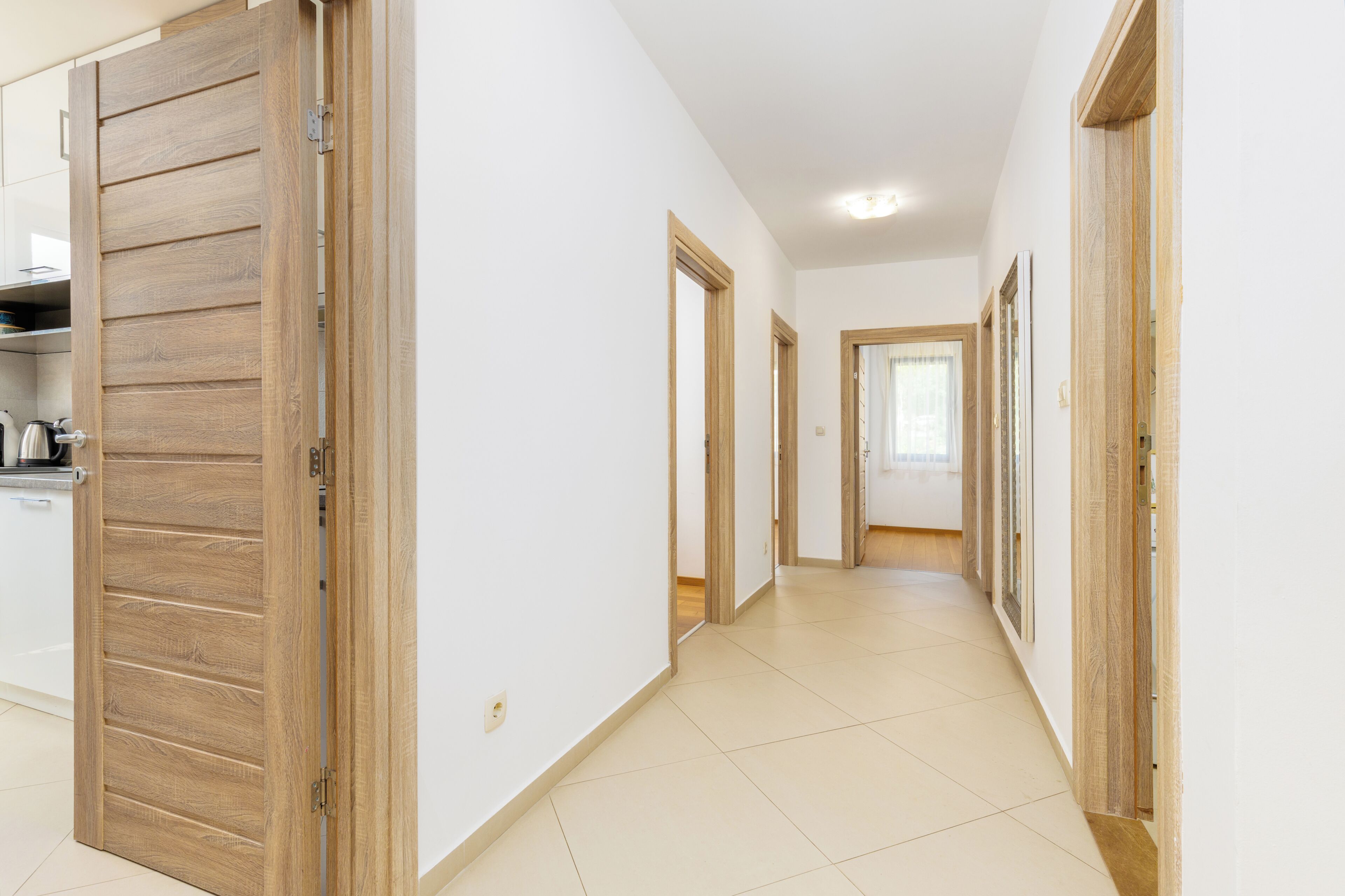 Un corridoio con porte in legno, pareti bianche e pavimento piastrellato.