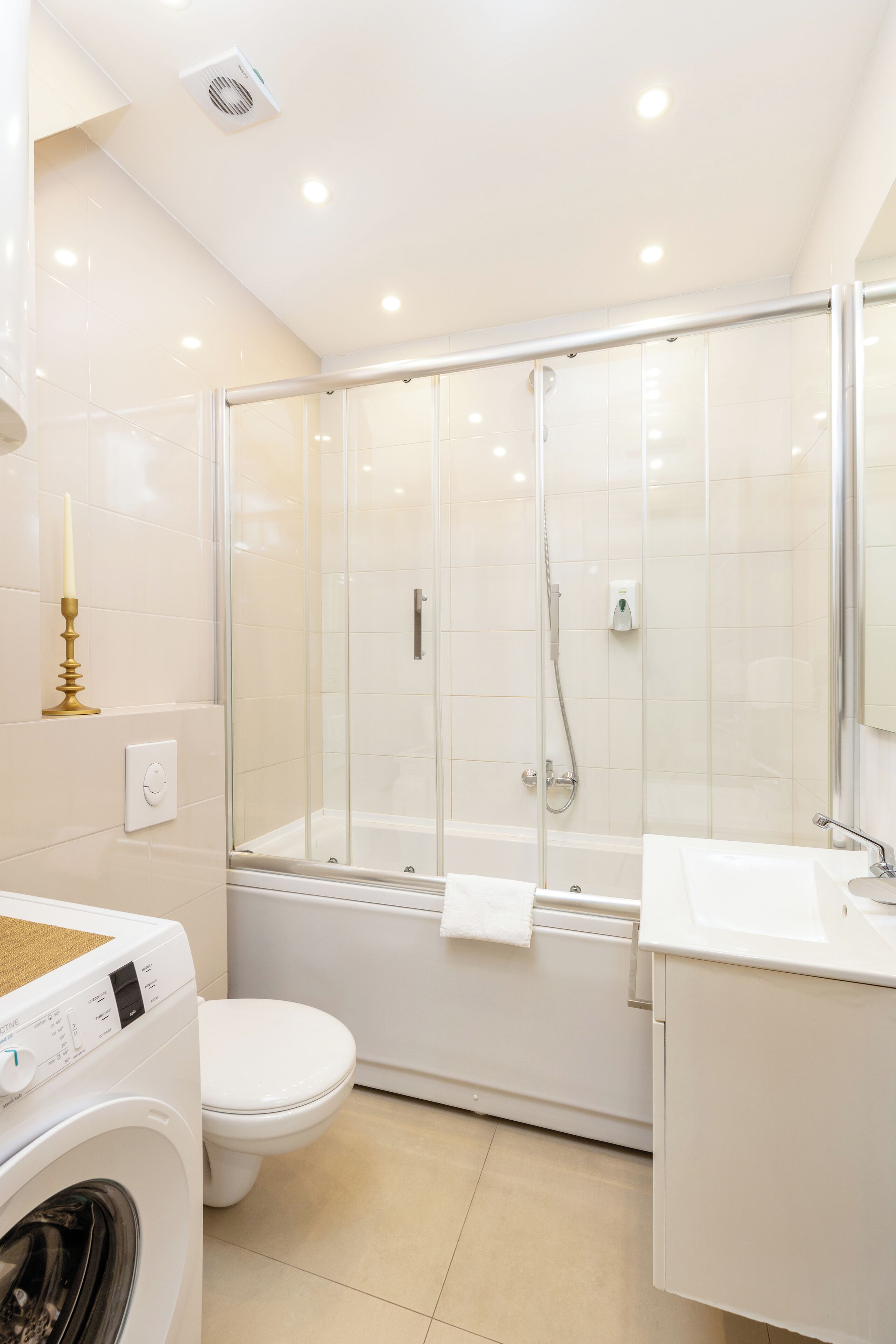 Ein modernes Badezimmer mit einer gläsernen Duschkabine, einer weißen Toilette, einer Waschmaschine und einem Waschbecken mit Spiegel.