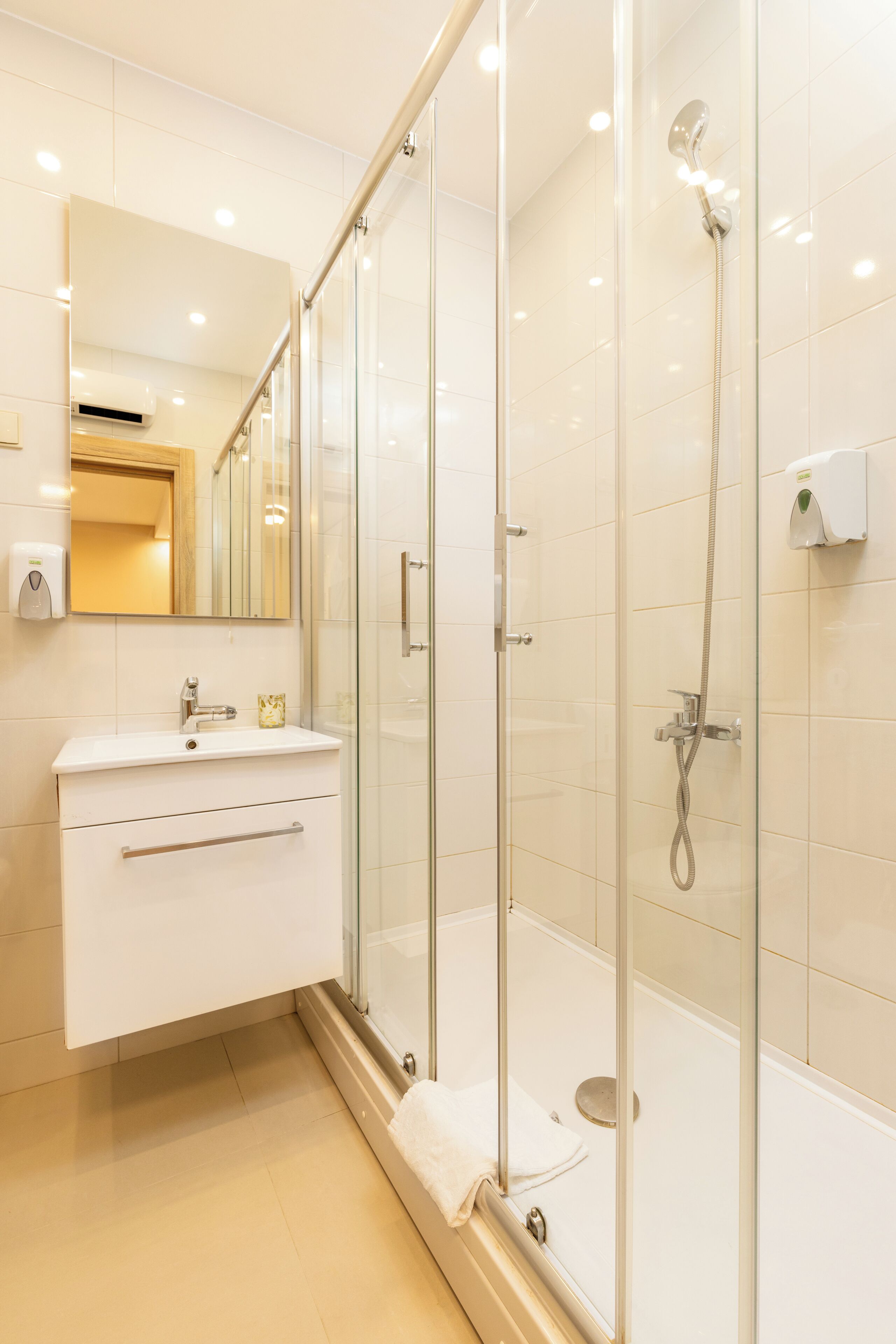 Un baño moderno con ducha de vidrio, tocador blanco y espejo sobre el lavamanos.