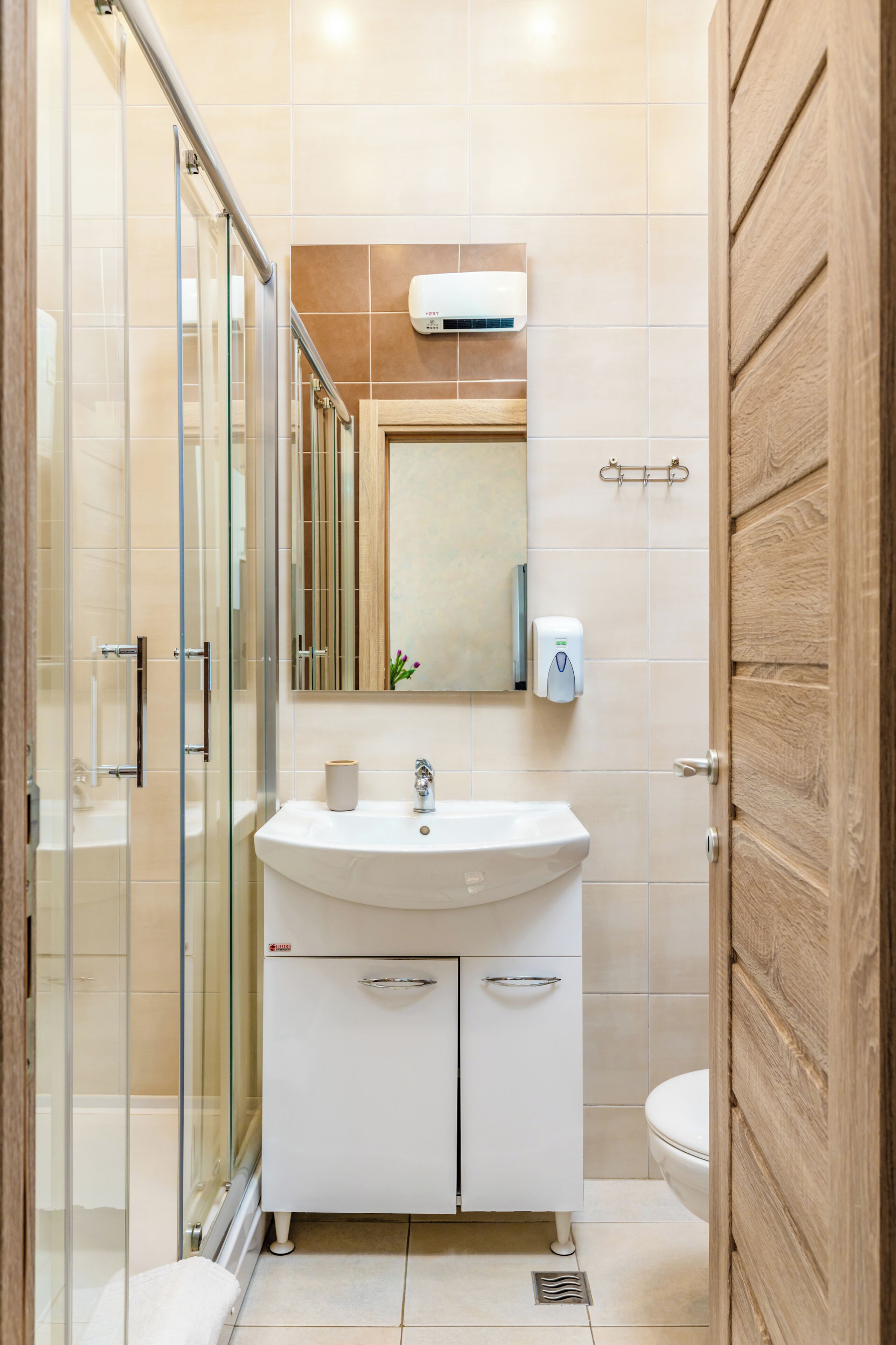 A modern bathroom with a glass shower enclosure, a white sink with a mirror above, and a wooden door.
