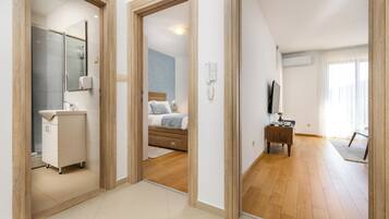 A modern hotel room with a bathroom, a bed, a TV, and a dining area.