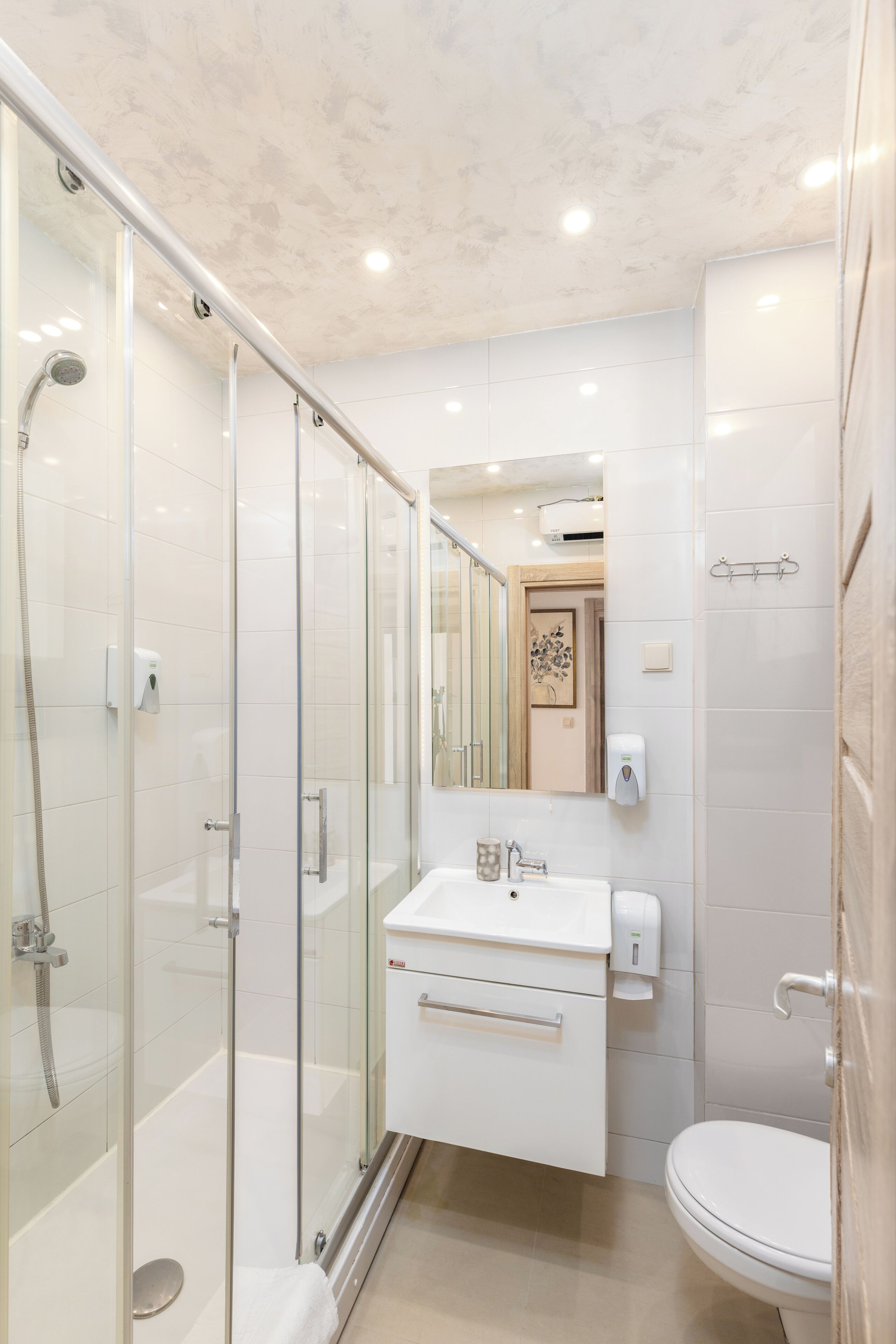 A modern bathroom with a glass-enclosed shower, a white sink with a mirror above, and a toilet.