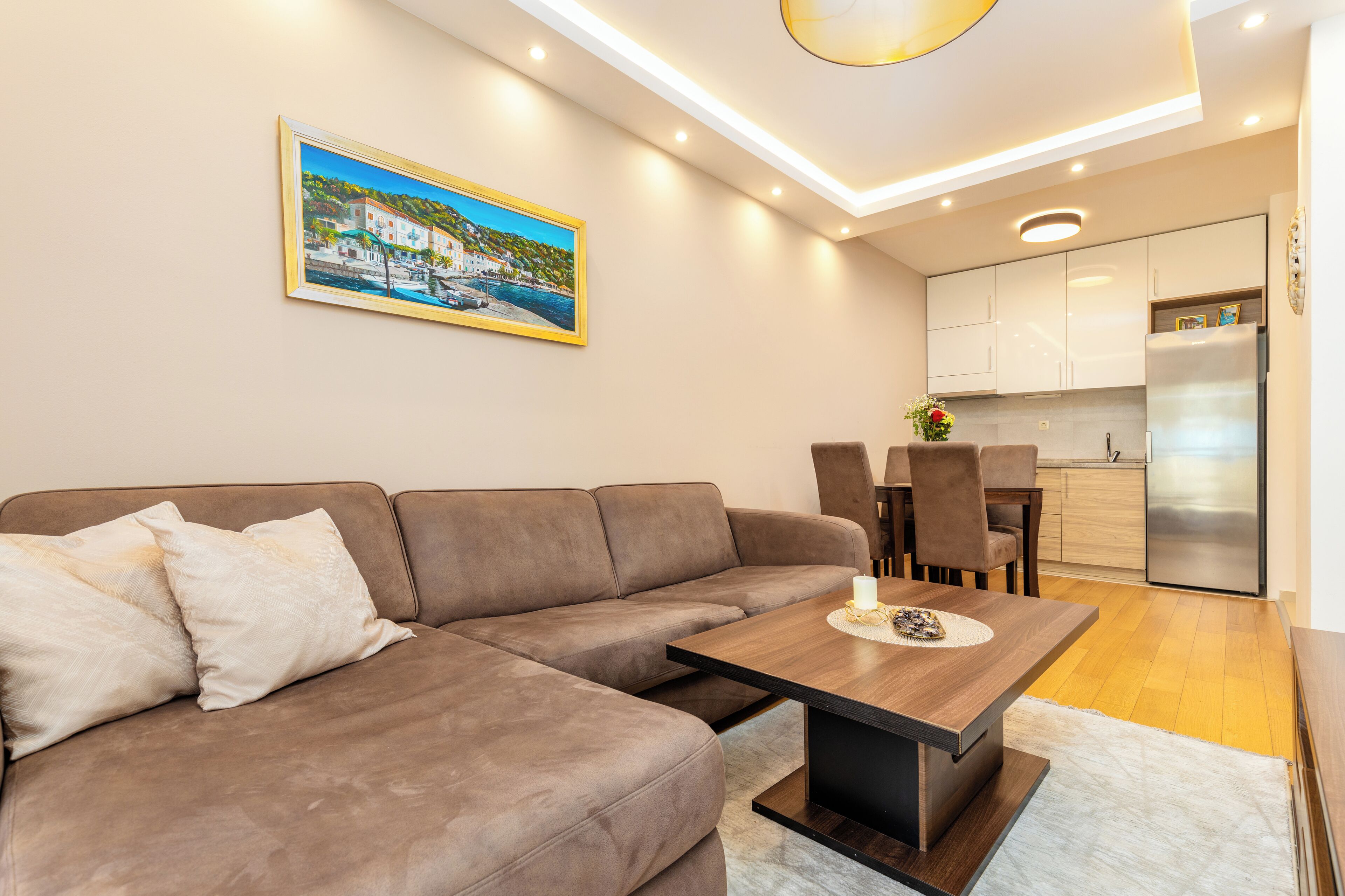 A modern living room with a brown sectional sofa, a wooden coffee table, and a painting of a coastal scene.