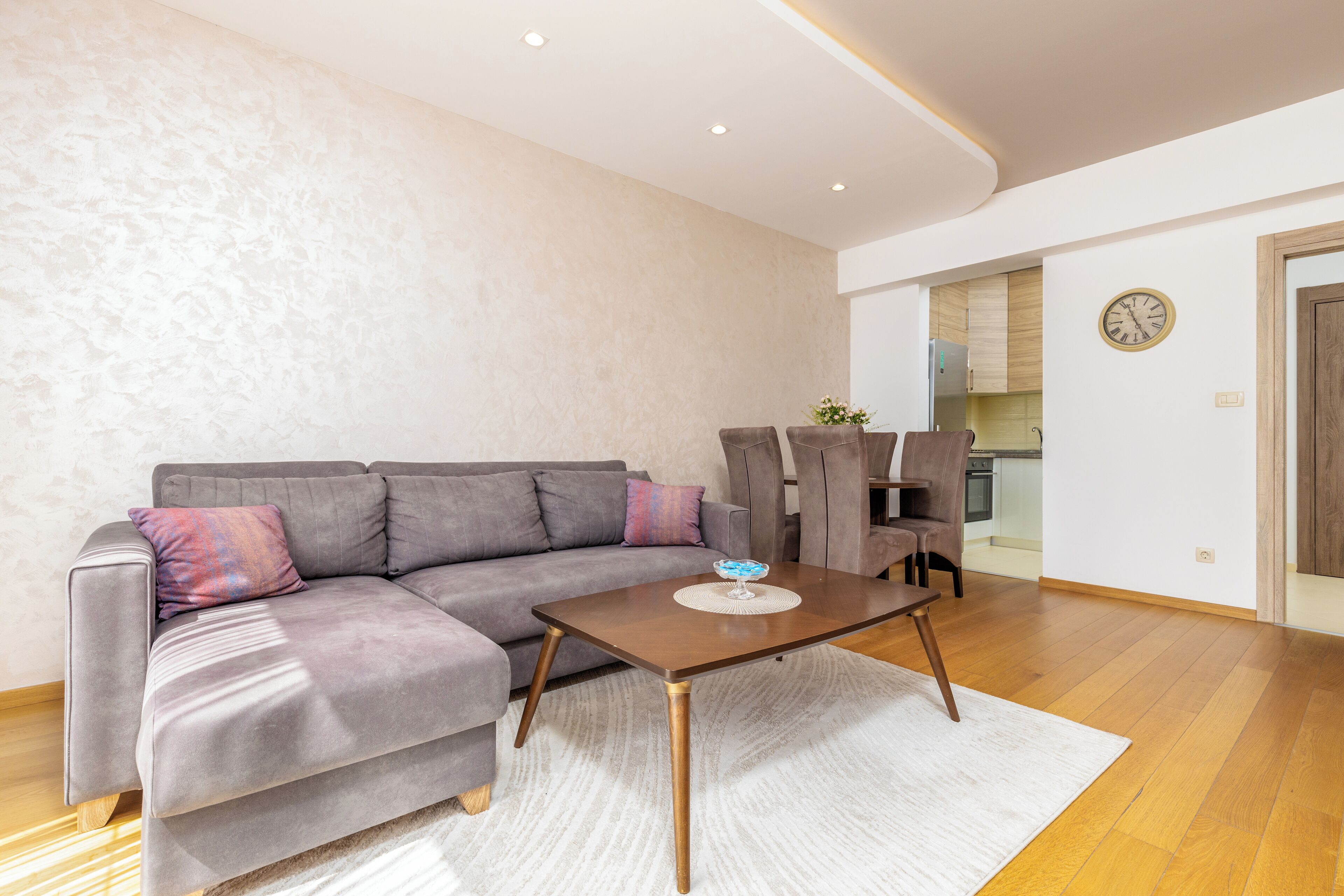 A modern living room with a grey sectional sofa, a wooden coffee table, and a white rug.