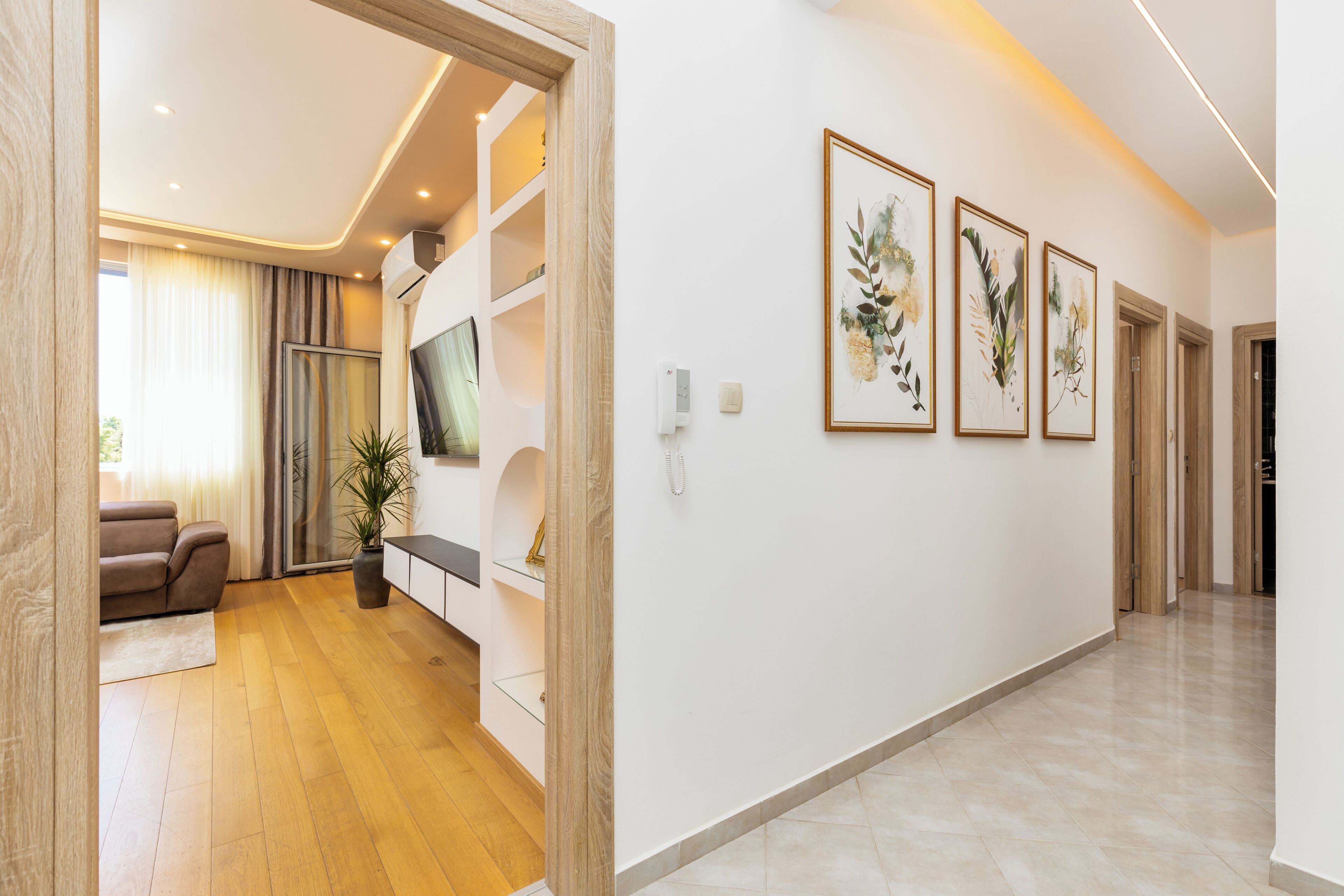 Un interno moderno con pavimento in legno, un divano, una televisione e opere d'arte botaniche incorniciate al muro.