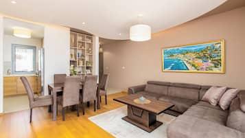 A modern living room with a dining area, a large sofa, and a painting of a coastal town.