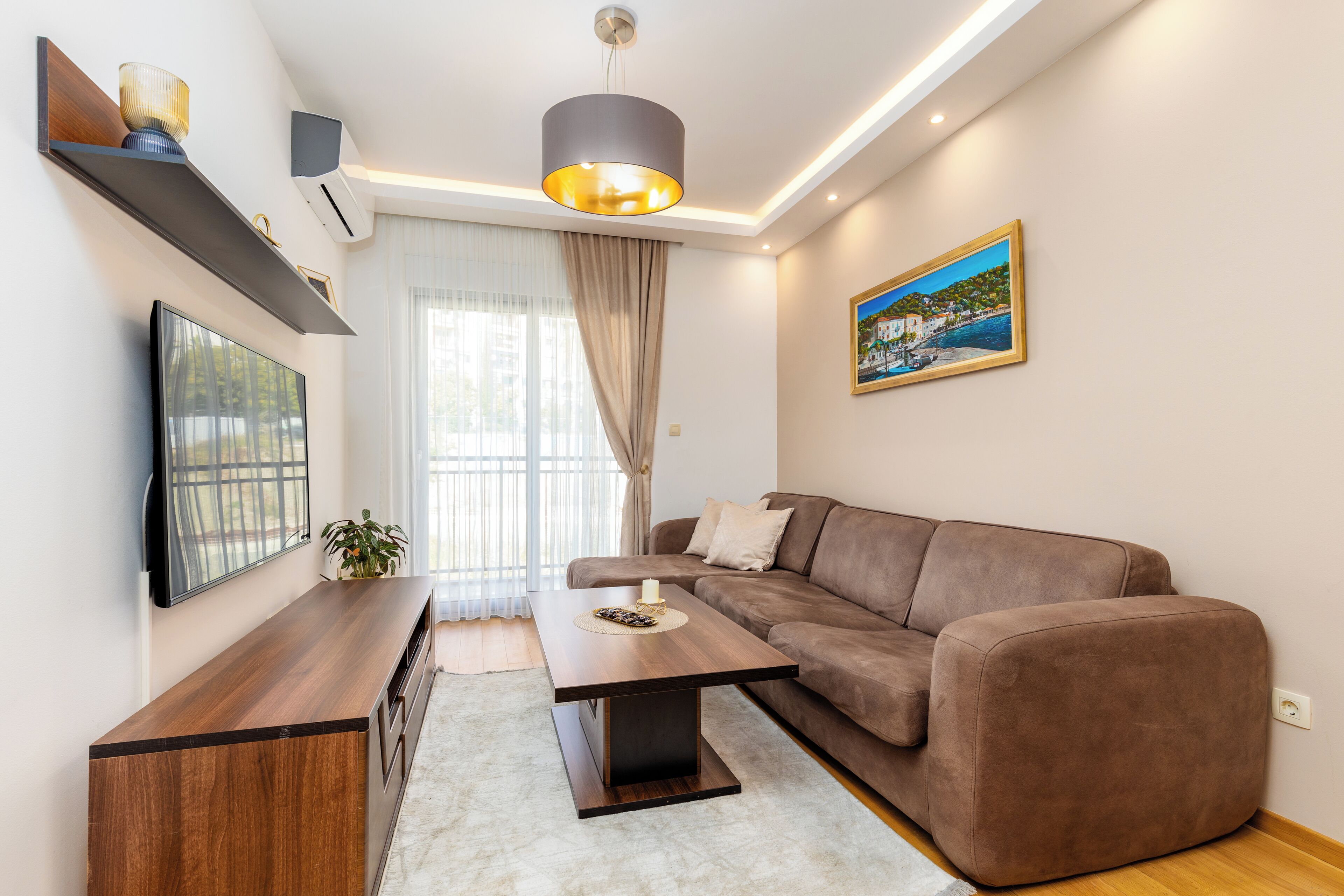 Un salon moderne avec un canapé marron, une table basse en bois, un téléviseur à écran plat et un tableau accroché au mur.