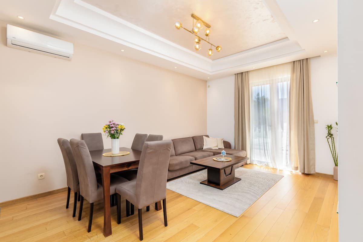 Ein modernes Wohnzimmer mit Essbereich, einer Couch, einem Couchtisch und einem großen Fenster mit Vorhängen.