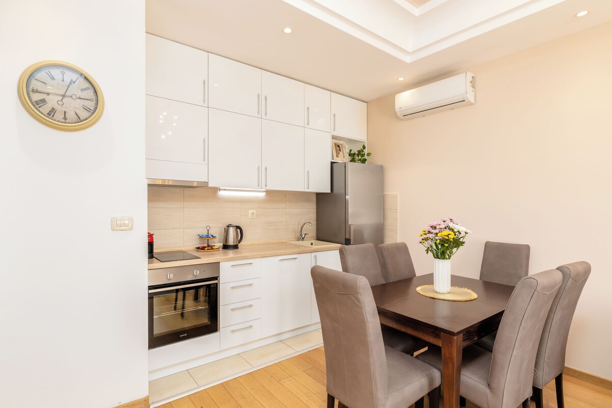 Een moderne keuken met witte kasten, een roestvrijstalen koelkast en een eettafel met stoelen.