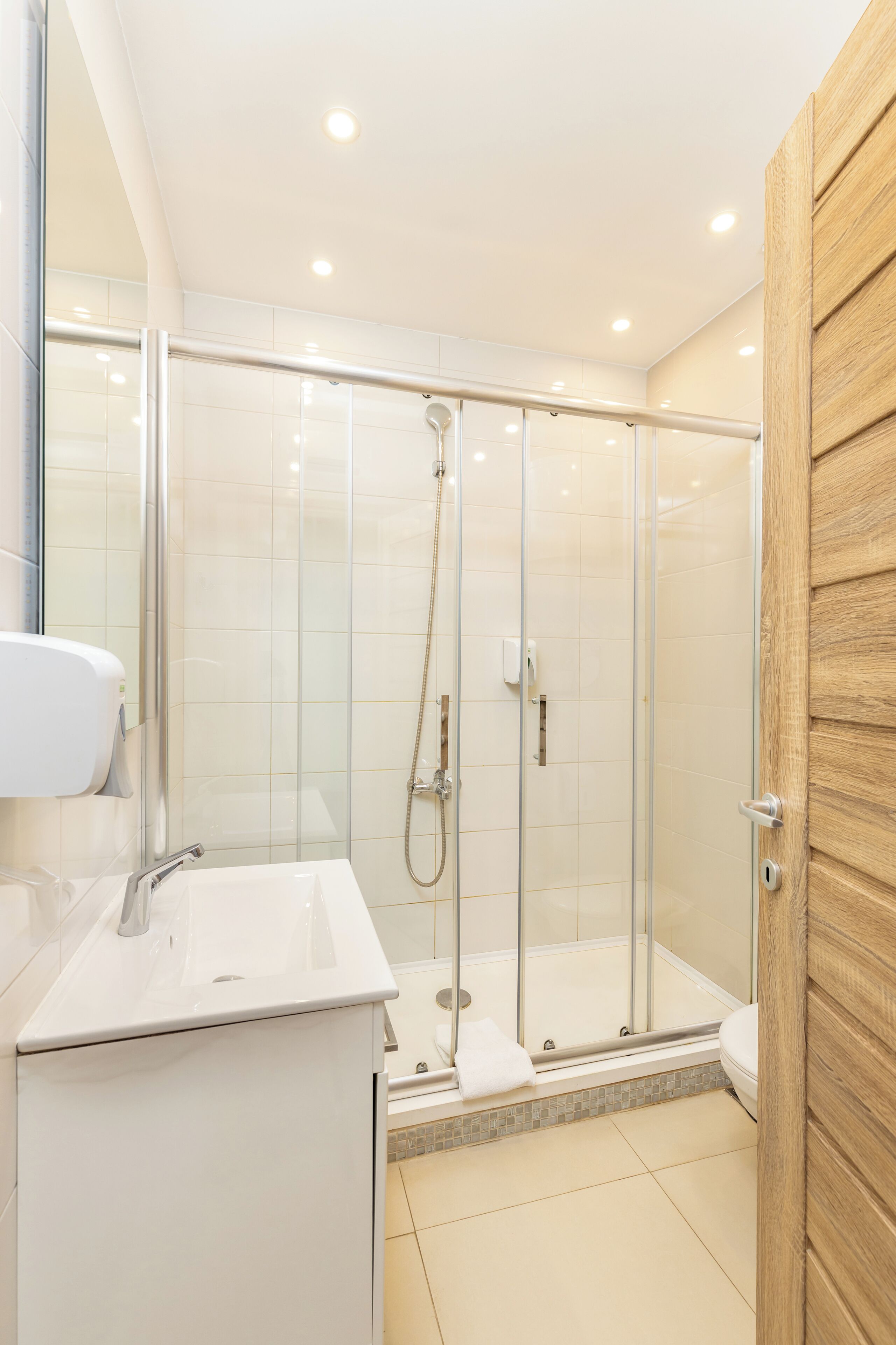 Un baño moderno con ducha de vidrio, un lavabo blanco y una puerta de madera.