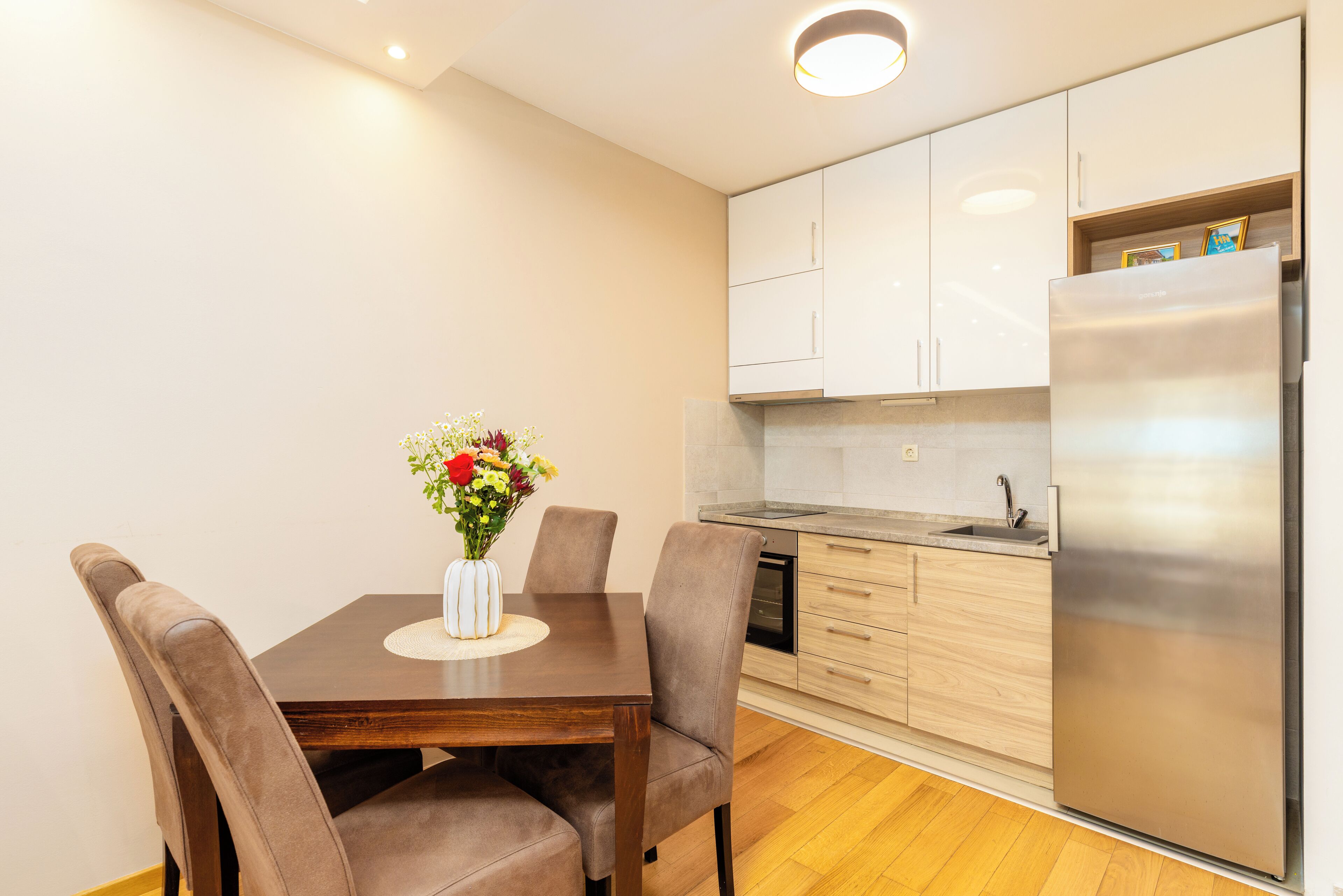 A modern kitchen with white cabinets, a stainless steel refrigerator, and a dining table with chairs.