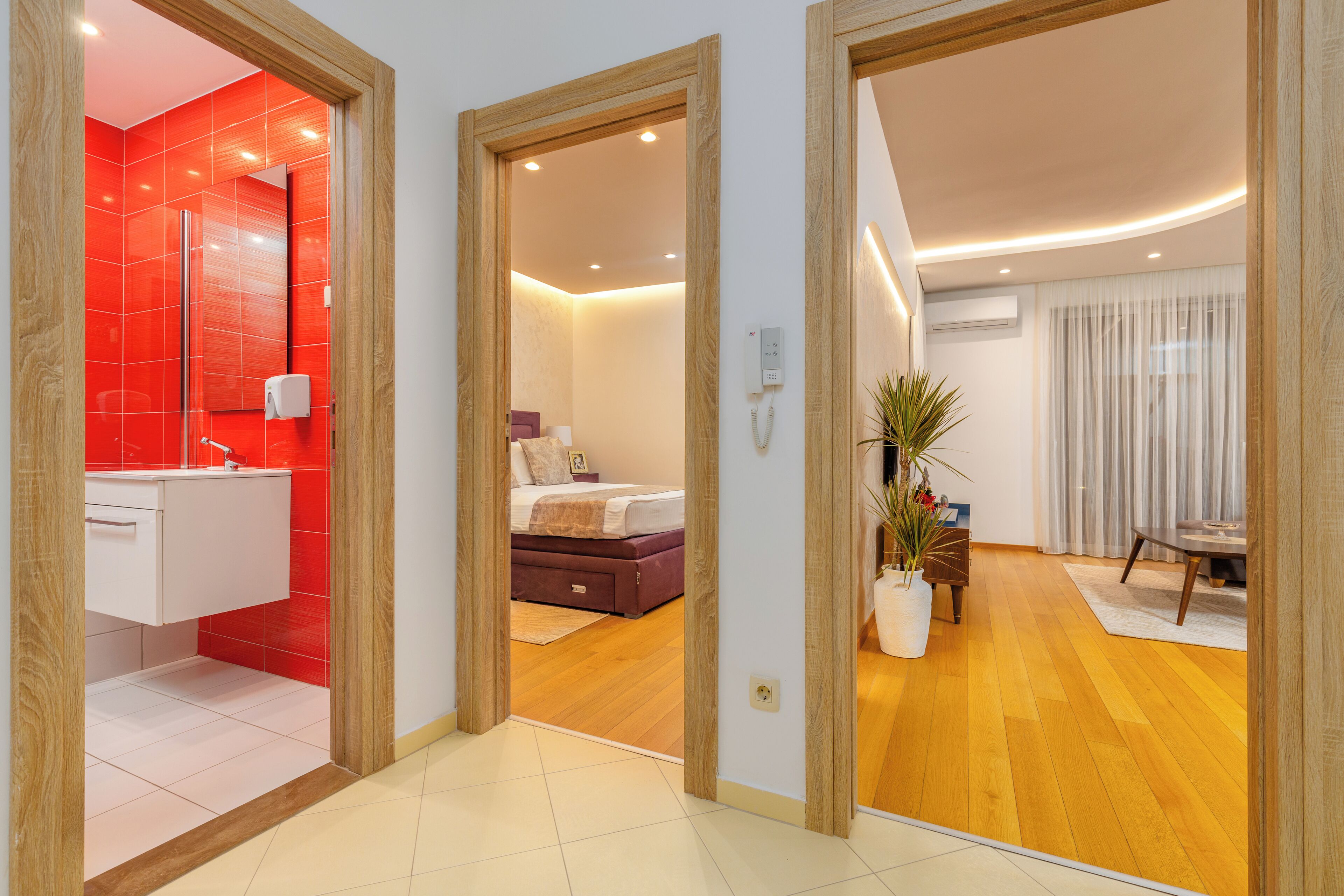 Una habitación de hotel moderna con un baño rojo, una cama con cabecera blanca y suelo de madera.