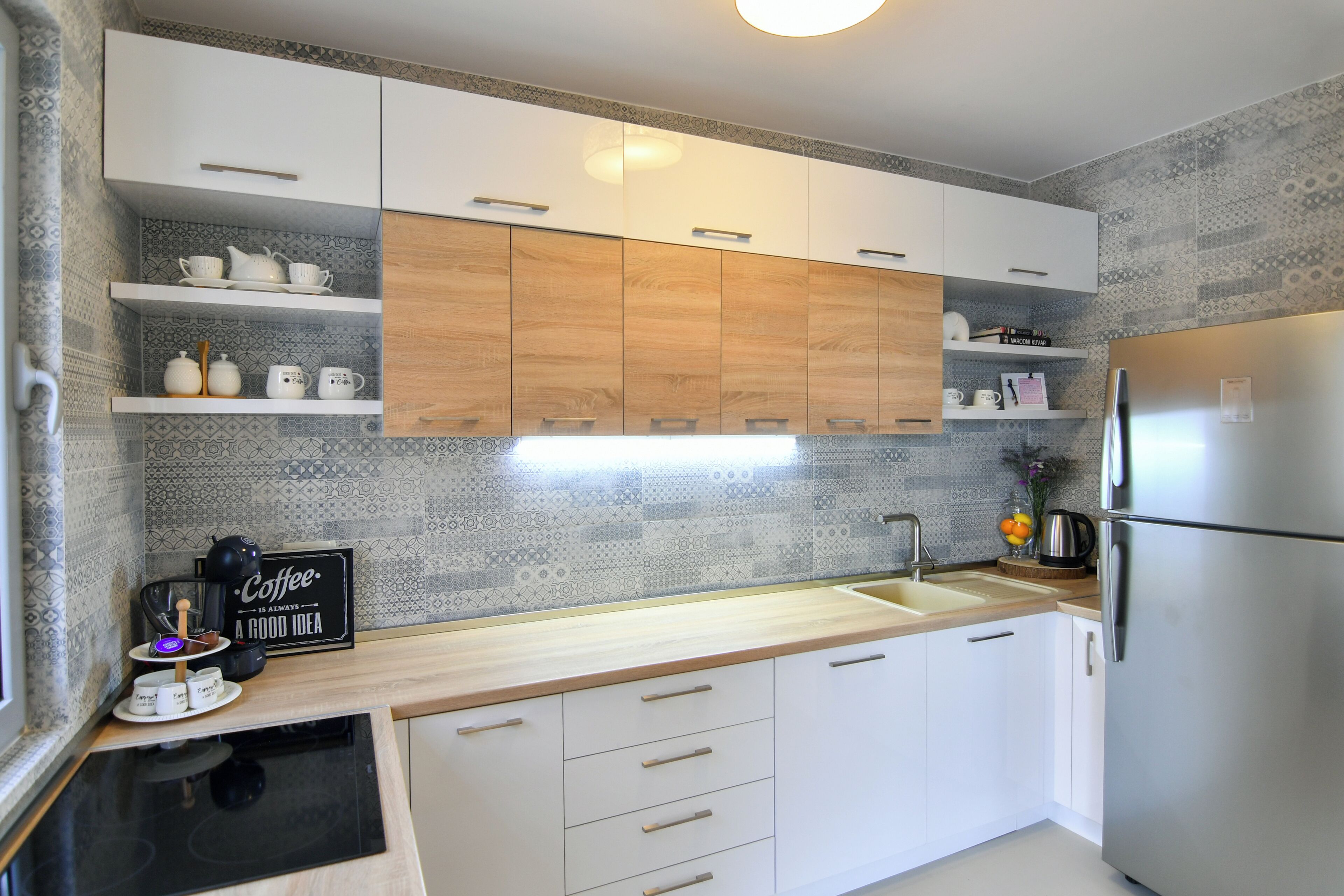 A modern kitchen with white cabinets, a stainless steel refrigerator, and a coffee machine.