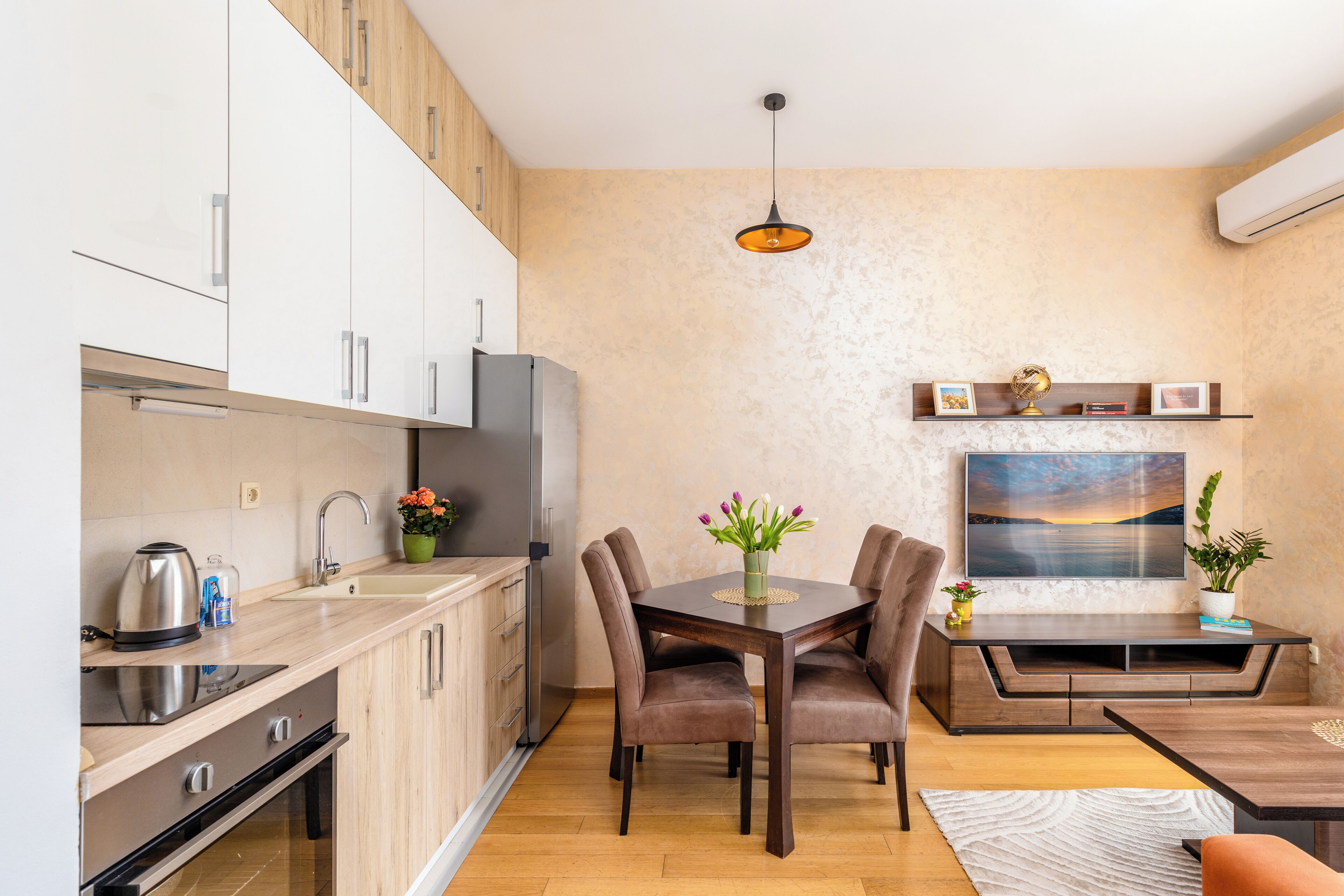 Cocina compacta con electrodomésticos modernos, comedor con mesa y sillas de madera, y sala de estar con sofá y televisor.