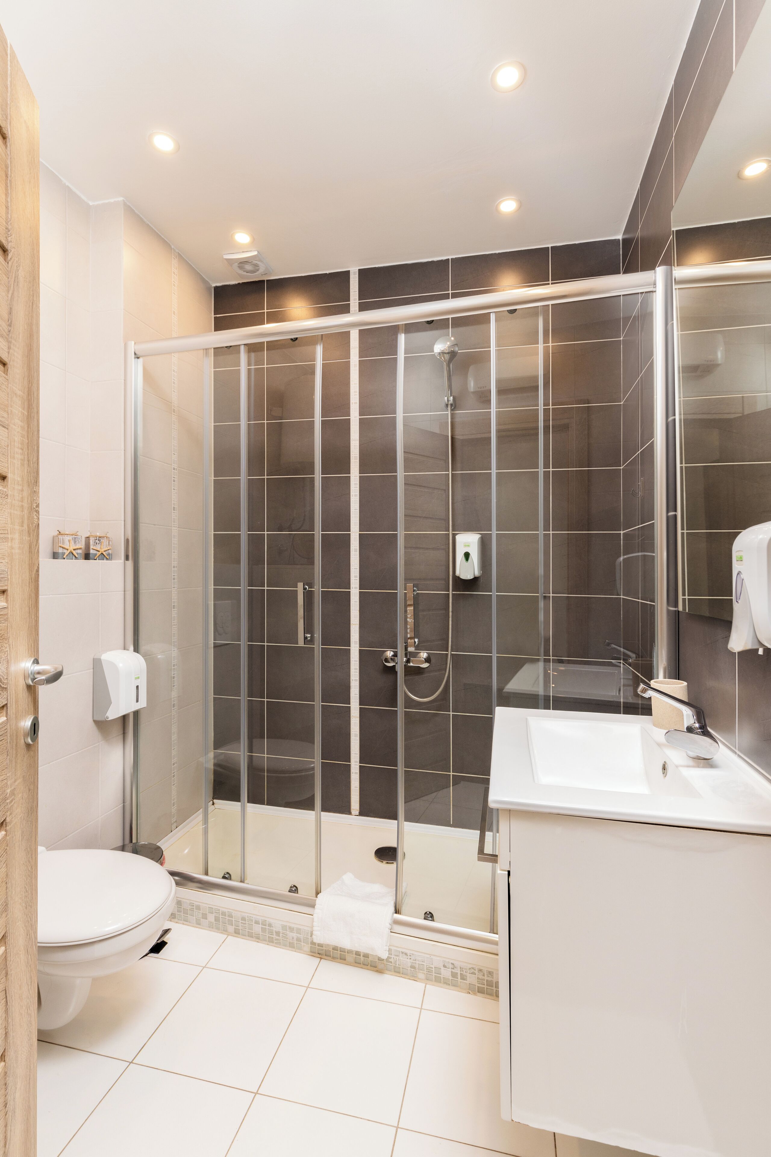 Et moderne badeværelse med en brusekabine i glas, et hvidt toilet og en vask med spejl.