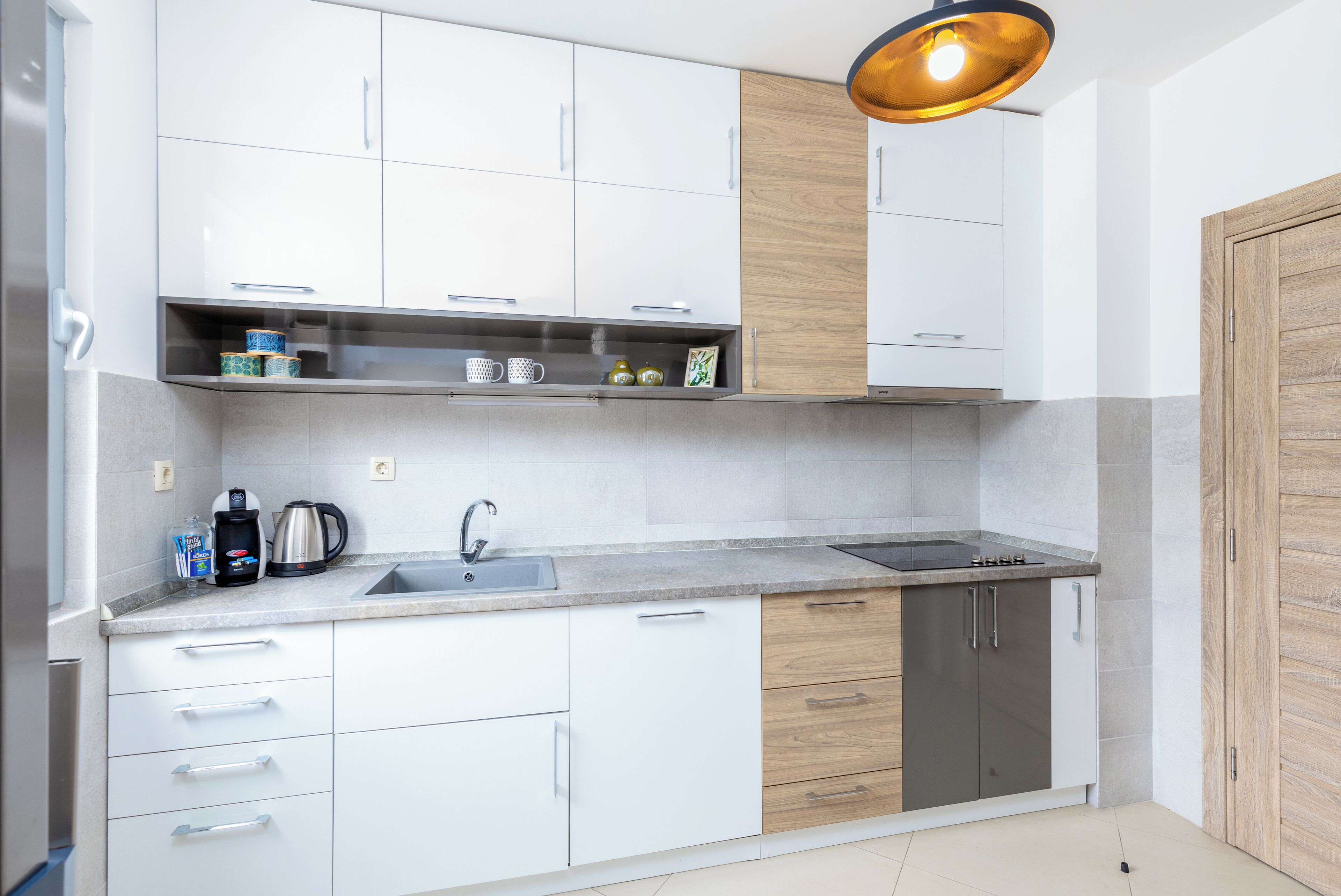 Une cuisine moderne avec des meubles blancs, un évier en acier inoxydable et une porte en bois.