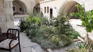 Une cour extérieure dotée d’un sol en pierre, d’une chaise en bois et d’une variété de plantes et de fleurs.