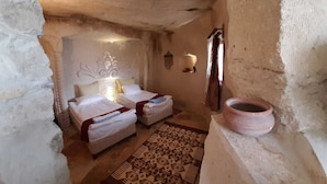 Une petite pièce rustique avec deux lits, un tapis à motifs, une lampe fixée au mur et un pot en argile.