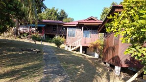 A residential area with houses featuring red roofs and wooden exteriors. A concrete path leads to the houses, surrounded by grass and trees. - Johan's Place (Tioman Island)