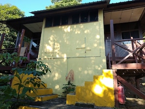 A building with a yellow exterior, a staircase leading to a porch, and a fire extinguisher near the steps. - Johan's Place (Tioman Island)
