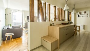 A modern kitchen with wooden beams, a central island, pendant lights, and a dining area with stools.