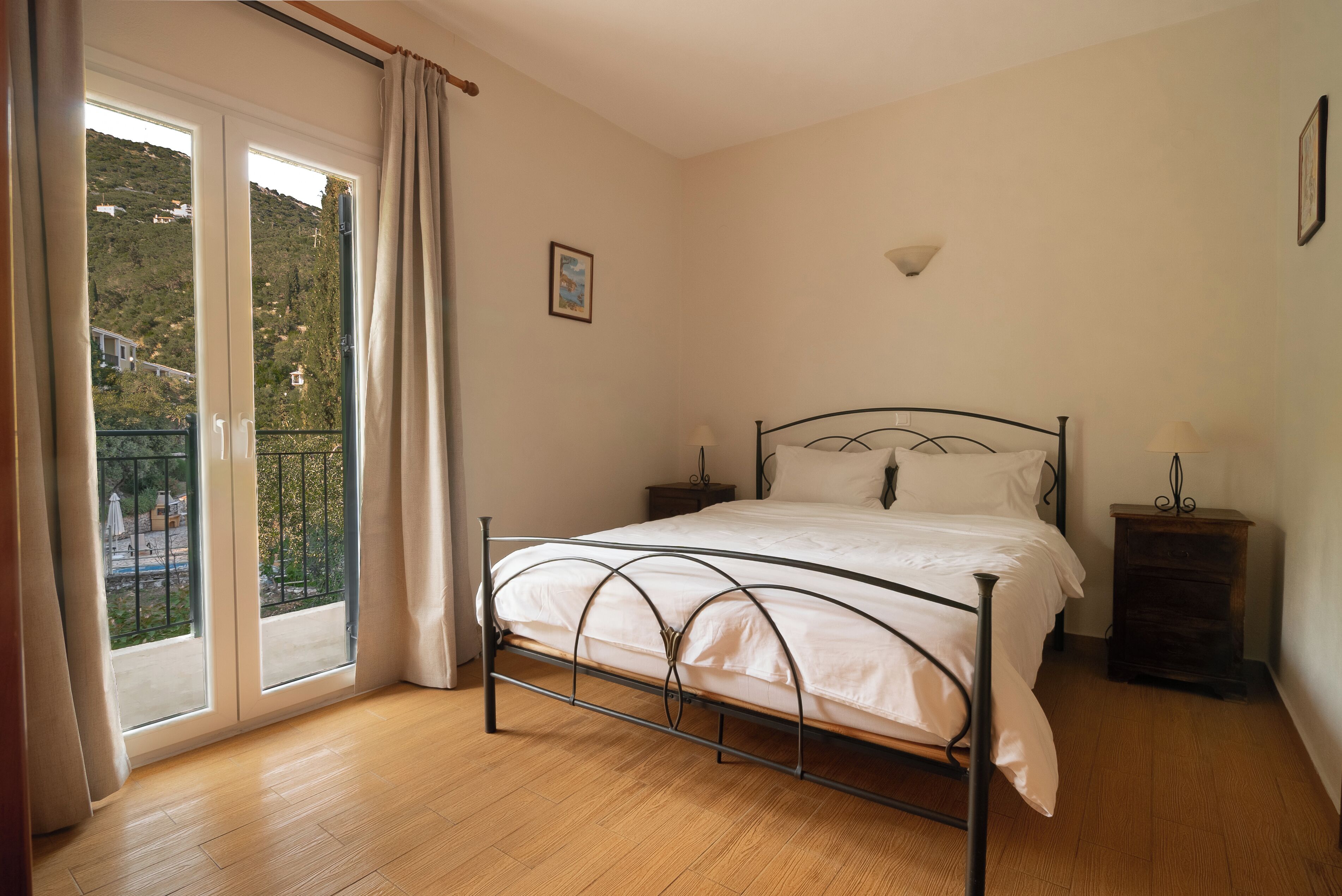 A bedroom with a bed, a nightstand, a window with curtains, and a view of a hillside.