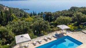 A pool area with lounge chairs and umbrellas, surrounded by trees and overlooking a body of water.