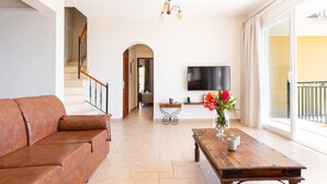 Un salon spacieux avec un canapé en cuir marron, une table basse en bois et un téléviseur fixé au mur.