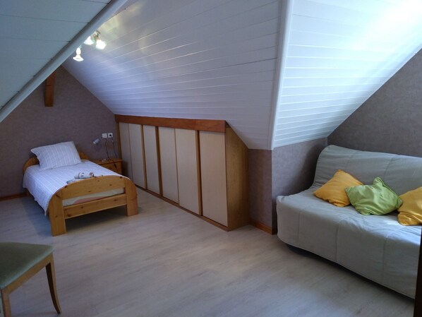 Un dormitorio con techo inclinado, una cama de madera, un sofá con cojines y un escritorio con una lámpara.