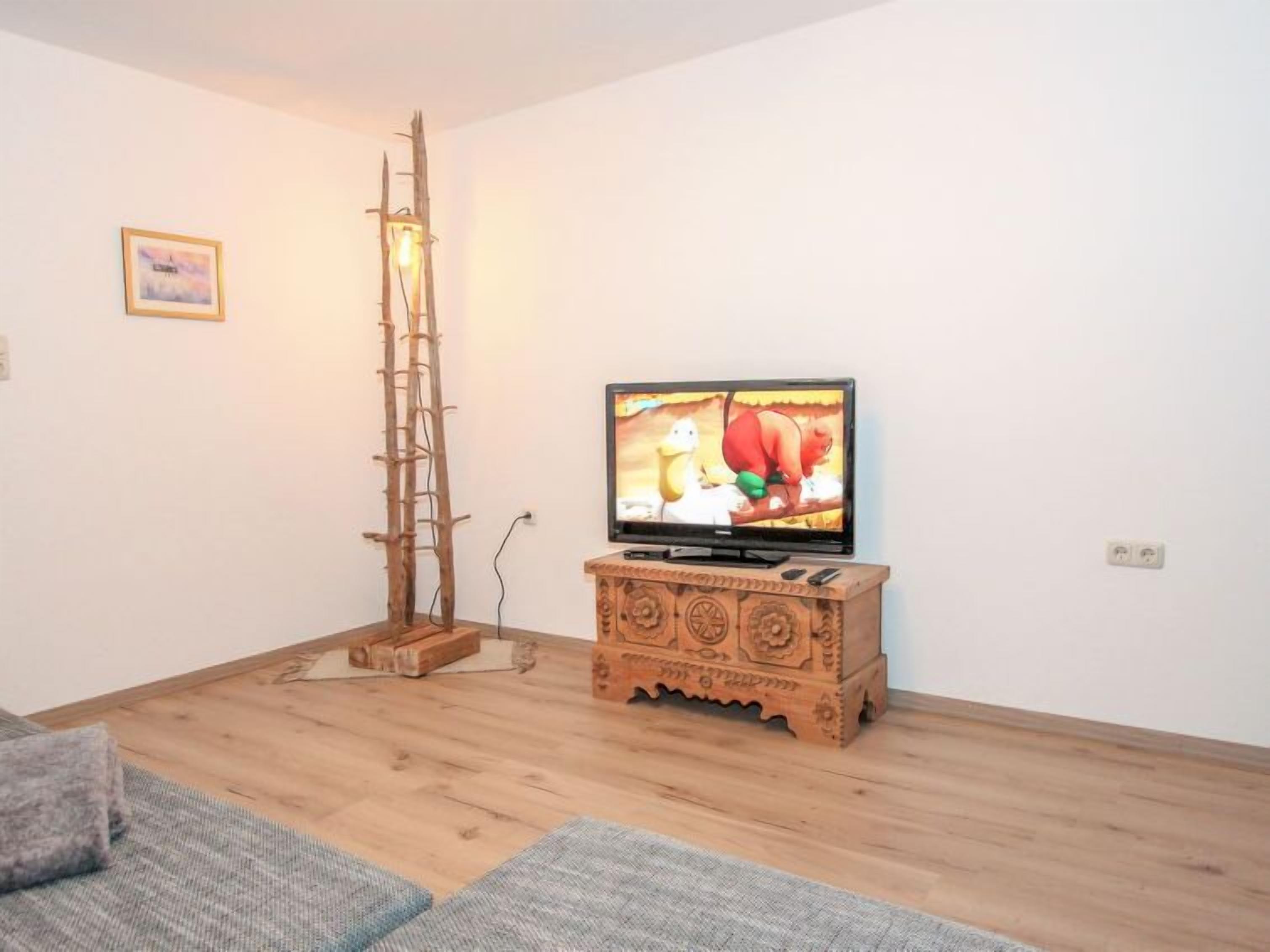 Una sala de estar con un mueble bajo de madera para el televisor, una escalera y una televisión mostrando una película animada.