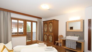 Une chambre à coucher avec un lit, une armoire en bois, une salle de bain avec un lavabo et un miroir, et une fenêtre avec des rideaux.