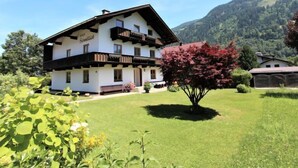 Un bâtiment à deux étages doté d’un balcon, entouré d’une pelouse bien entretenue et ayant une chaîne de montagnes en toile de fond.