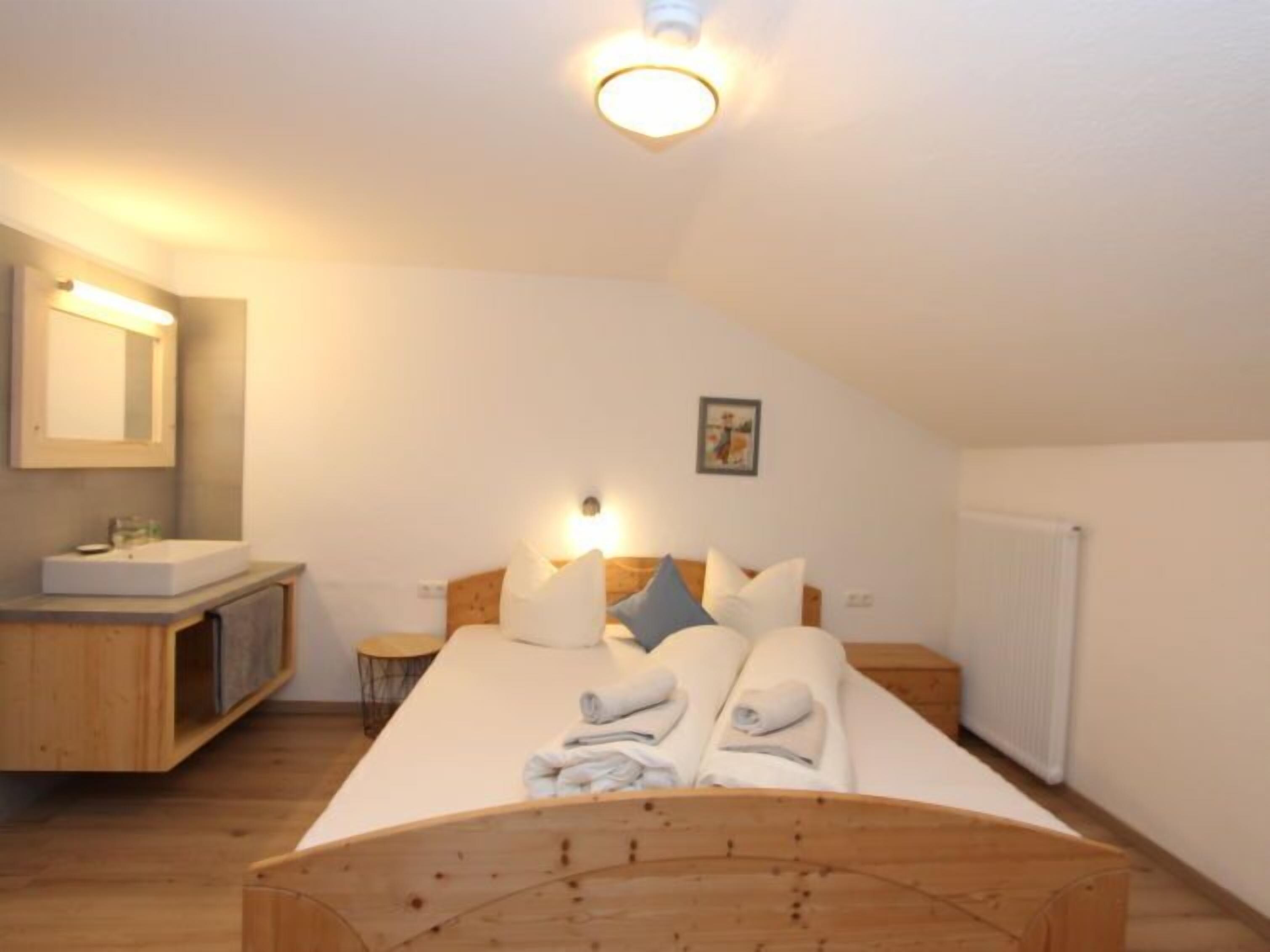 A bedroom with a wooden bed, a bedside table, a nightstand, a mirror, a radiator, and a small stool.