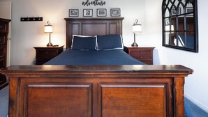 Ein Schlafzimmer mit einem großen Holzbett, zwei Nachttischen mit Lampen, einem an der Wand befestigten Spiegel und einem Schild über dem Bett mit der Aufschrift 'adventure'.