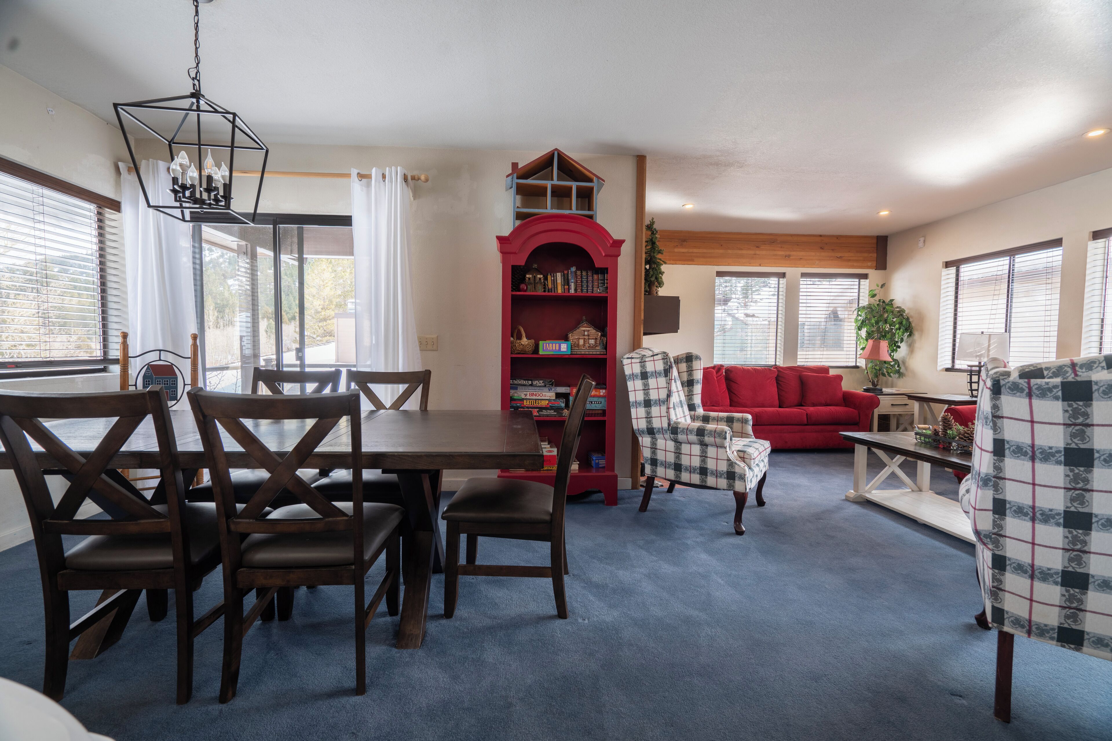 A living room with a dining table, chairs, a red bookshelf, a red sofa, and a patterned armchair.