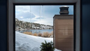 Ein Fenster mit Blick auf eine verschneite Landschaft, einen See und ein Gebäude mit Schornstein.